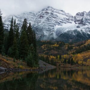 view of a lake surronded by fall colored trees and a snowy capped mountain in the background
