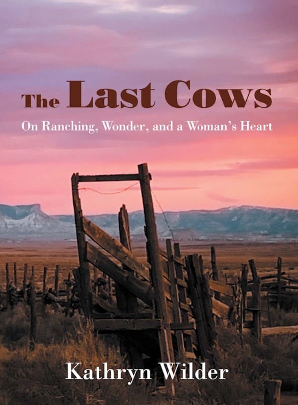 A book cover titled "The Last Cows" by Kathryn Wilder. The subtitle reads "On Ranching, Wonder, and a Woman's Heart." The image depicts a rustic, weathered wooden fence or corral structure in the foreground, set against a vast, dry Western landscape with distant mountains under a dramatic sunset sky in shades of purple, pink, and orange.