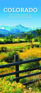 Official Guide to Colorado Scenic and Historic Byways brochure cover featuring a vibrant landscape of rolling yellow meadows in the foreground, lush green hills in the midground, and jagged, snow-capped mountain peaks under a clear blue sky in the background.