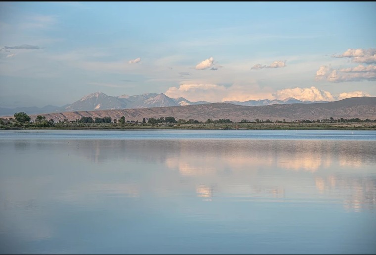 Panoramic view of Sweitzer Lake with distant mountains and white clouds reflecting on the calm blue water.