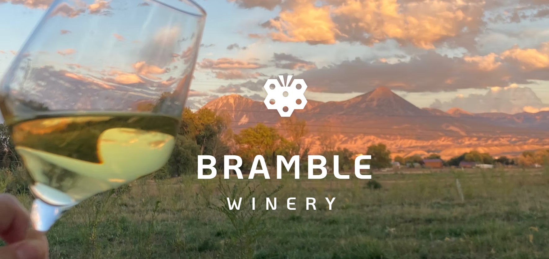 Wine Glass of White with a background of sunset and mountains and Bramble Winery Logo