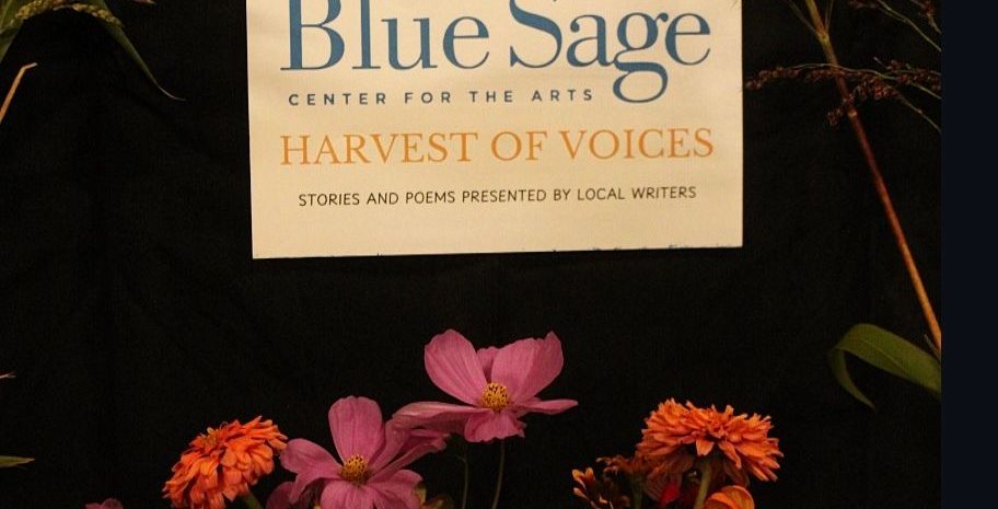 A white sign on a dark background reads "Blue Sage Center for the Arts Harvest of Voices." Colorful fall flowers, including orange and pink zinnias, bloom beneath the sign.