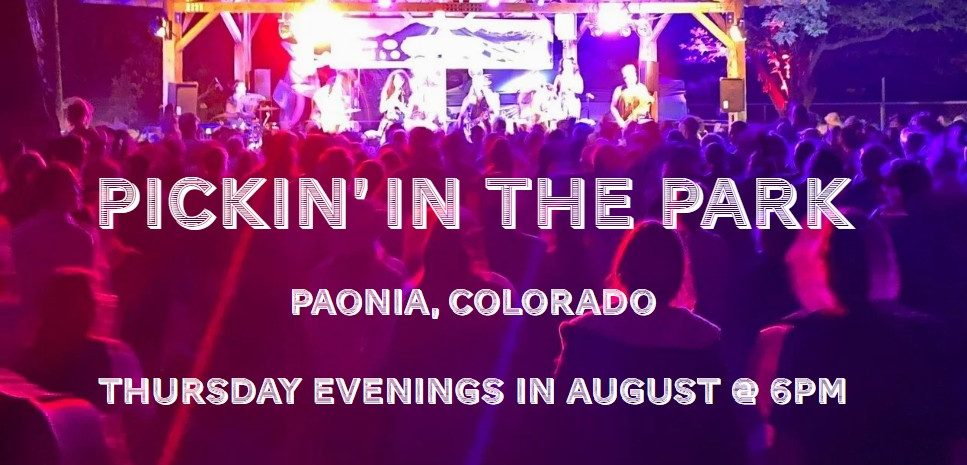 A large crowd at an outdoor night concert in a park. A band performs on a bright purple-lit stage under a wooden pavilion. Text reads: Pickin' in the Park.