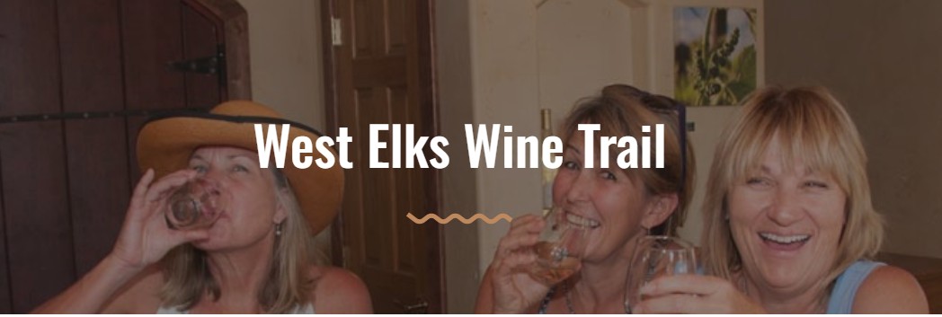 Three women smiling and laughing while enjoying glasses of wine at a West Elks AVA winery. Text reads "West Elks Wine Trail."