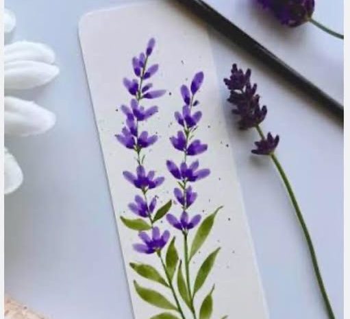 Close-up photo of a hand-painted watercolor bookmark featuring delicate purple lavender stems and green leaves resting on a white table next to paintbrushes and real lavender sprigs.