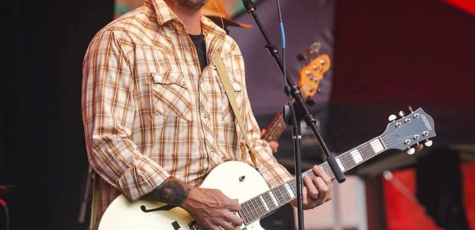 Musician James "Papa Bear" Williams singing into a microphone while playing a white semi-hollow body electric guitar live on stage