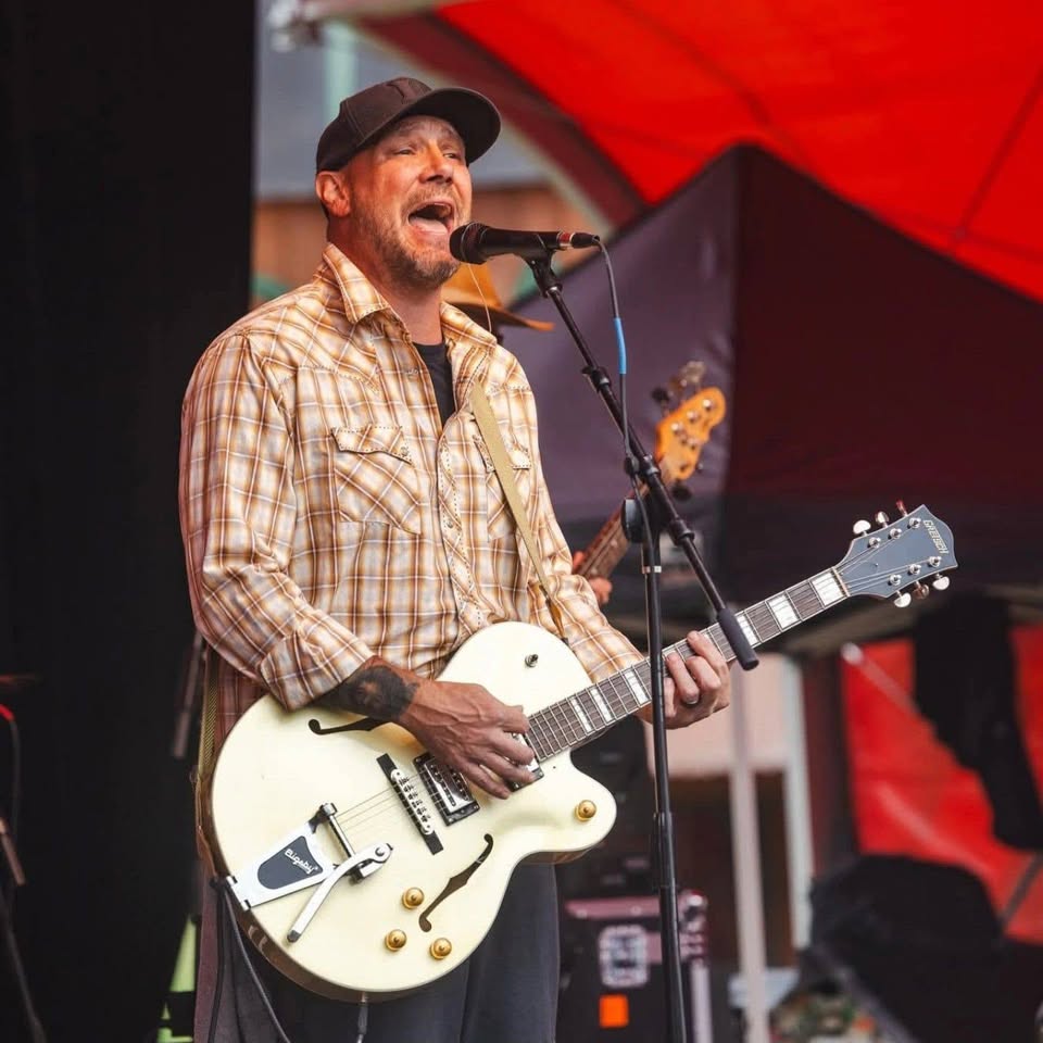 Musician James "Papa Bear" Williams singing into a microphone while playing a white semi-hollow body electric guitar live on stage