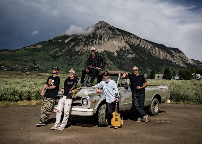 Band promotional photo of Mountain Jam, a five-piece rock band posed around a vintage pickup truck in front of a scenic mountain backdrop in Crested Butte, CO.